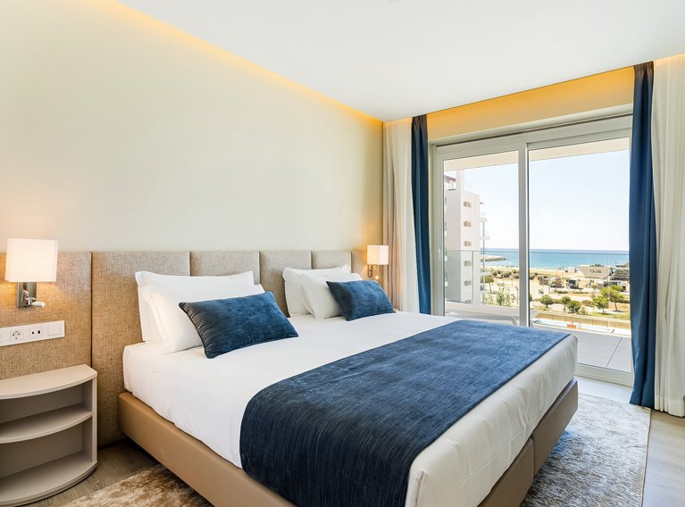 Quarto com cama de casal, varanda e vista para o mar com espreguiçadeiras, banheira no quarto, nos apartamentos de luxo do Dom Pedro Residences em Vilamoura, Algarve.